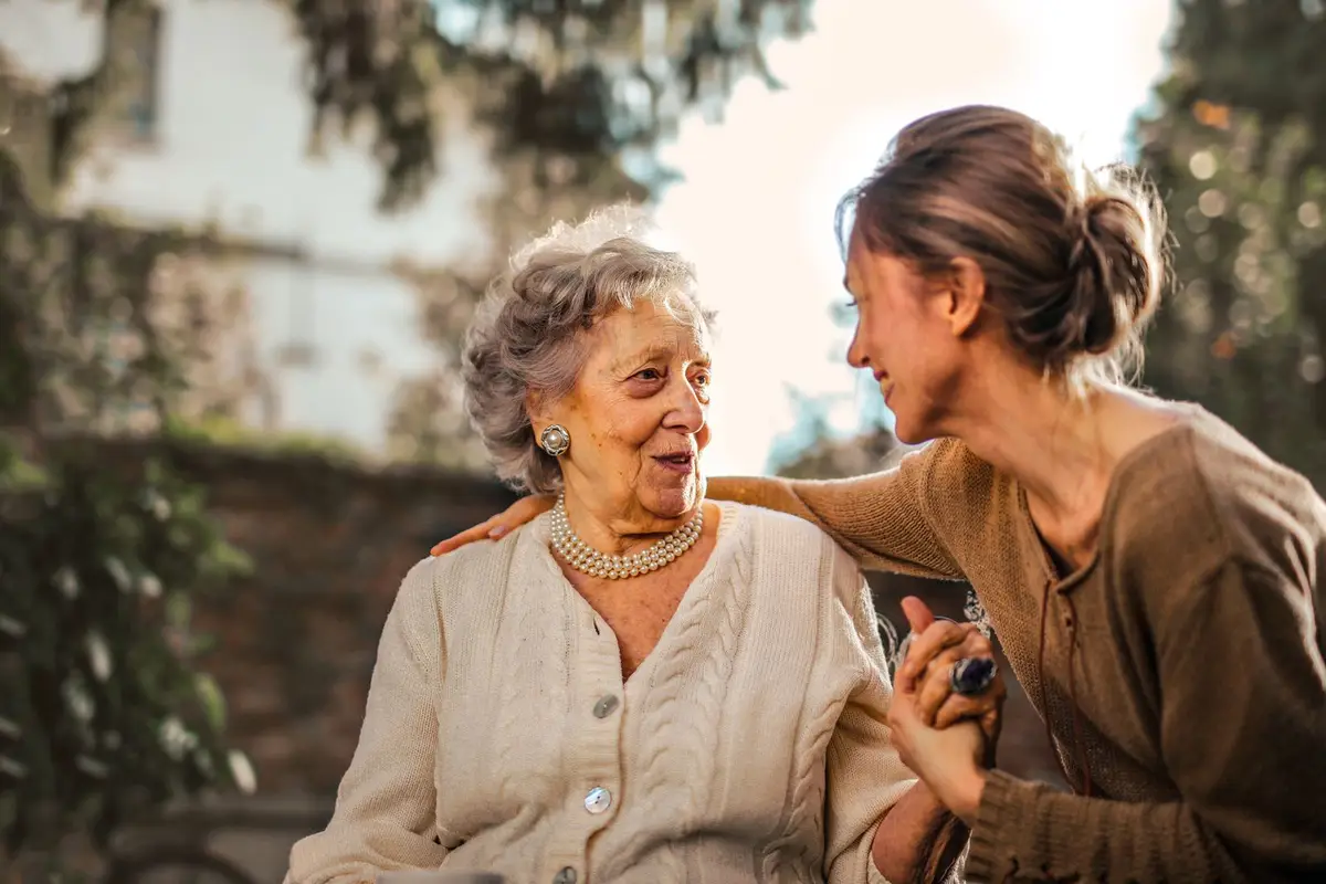 An older woman and a younger woman talking closely in a sunny garden. Not a client of Immaculate Heart Care and Cleaning Services.